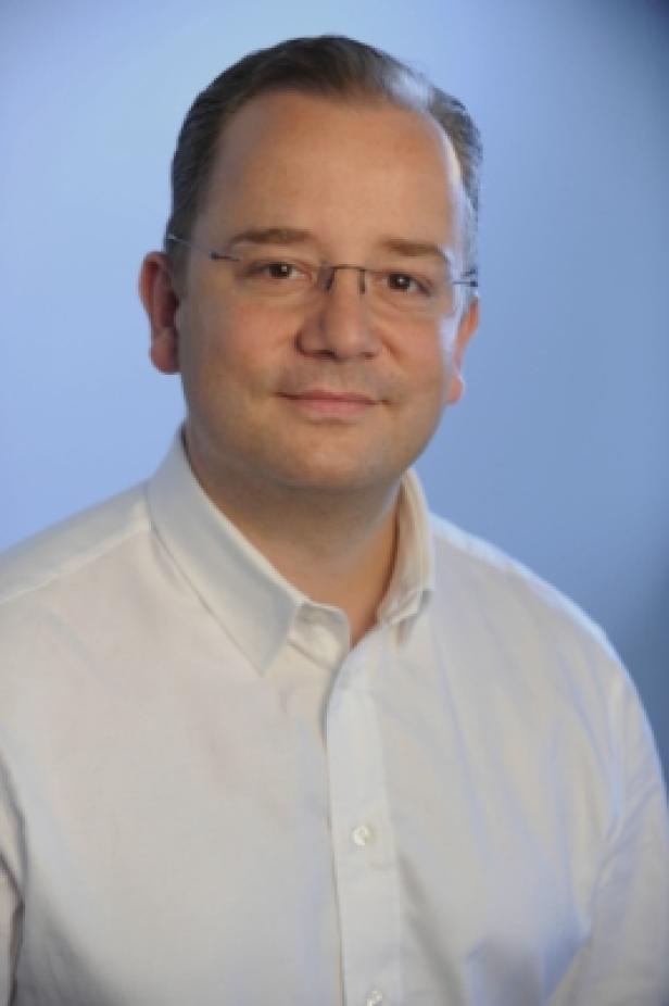 Michael Göls, Geschäftsführer MPG Austria (c: outline pictures) Ein Mann mit Brille und weißem Hemd vor einem blauen Hintergrund.