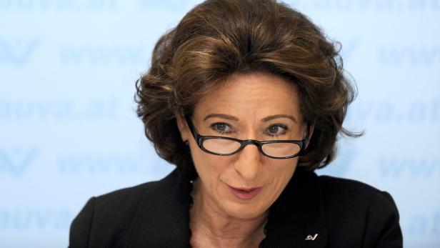 Nahaufnahme einer Frau mit Brille und braunen Haaren vor einem hellblauen Hintergrund.