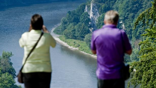 Zwei Personen blicken auf einen Fluss und eine bewaldete Landschaft.