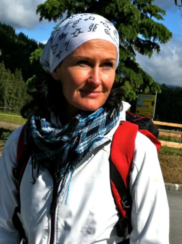 Eine Frau mit Kopftuch und Rucksack steht im Freien.