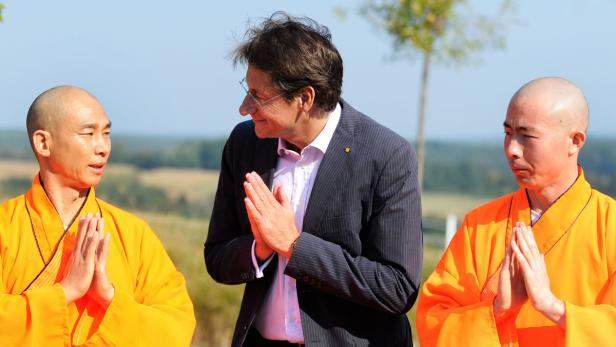 Ein Mann in Anzug steht zwischen zwei buddhistischen Mönchen.