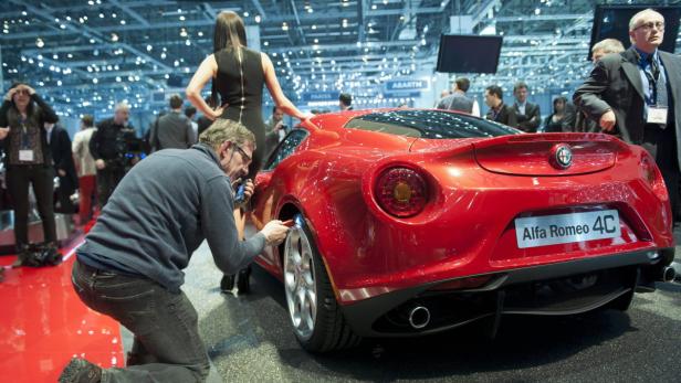 Ein roter Alfa Romeo 4C wird auf einer Automesse von einem Mann poliert.