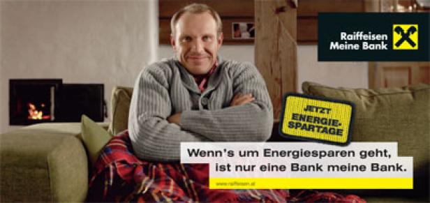 Raiffeisen-Kampagne Energiesparen mit Hermann Maier/24-Bogen-Plakat Ein Mann sitzt entspannt auf einem Sofa mit einer Decke und wirbt für die Raiffeisenbank.
