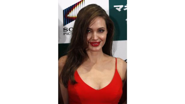 Angelina Jolie in einem roten Kleid mit roten Lippenstift vor einer Sponsorenwand.
