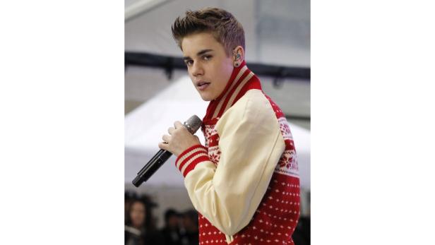 Justin Bieber hält ein Mikrofon und trägt eine rote Strickjacke.
