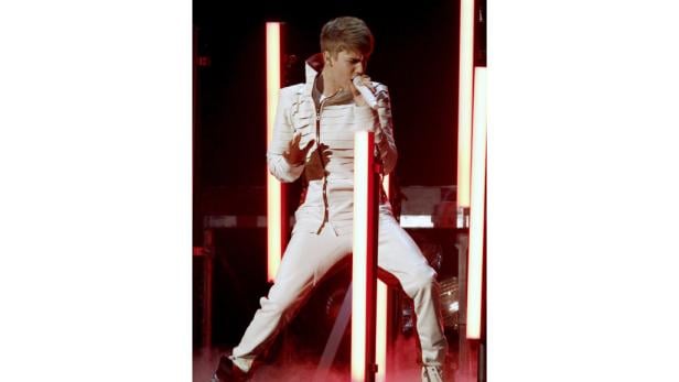 Justin Bieber singt in einem weißen Anzug auf einer Bühne mit roten Lichtern.