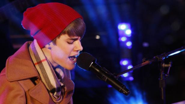 Justin Bieber singt mit roter Mütze und Schal in ein Mikrofon.