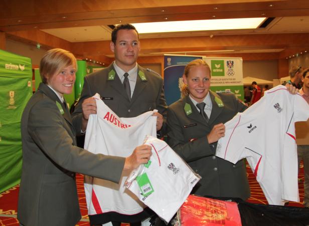 Drei Personen in Uniformen präsentieren T-Shirts des österreichischen Olympiateams.