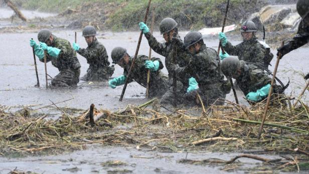 Soldaten durchsuchen im Regen knietiefes Wasser mit Stöcken.