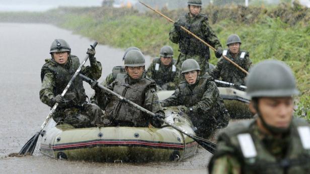 Eine Gruppe Soldaten in Tarnuniformen paddelt in einem Schlauchboot durch überflutetes Gebiet.