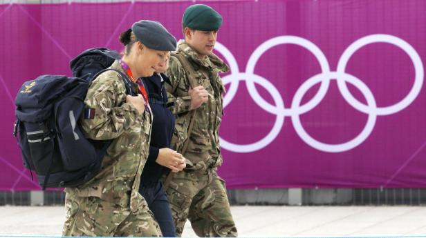 Zwei Personen in Militäruniformen gehen vor dem Hintergrund der Olympischen Ringe entlang.