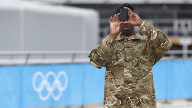 Ein Soldat in Uniform fotografiert mit seinem Smartphone die olympischen Ringe.