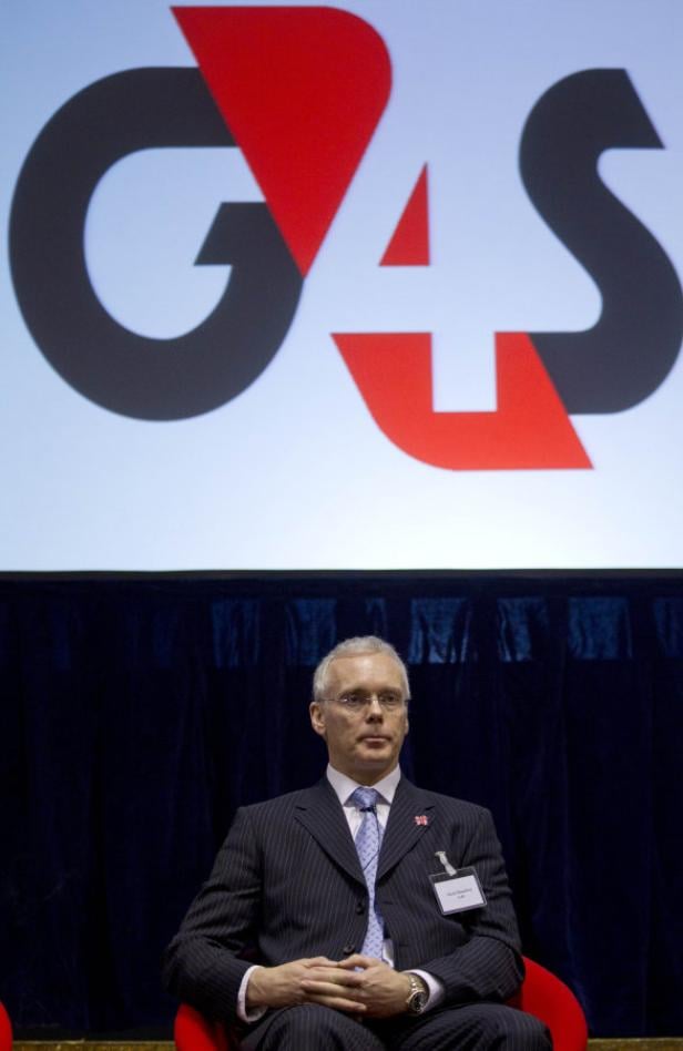 Ein Mann im Anzug sitzt vor einem Bildschirm mit dem G4S-Logo.