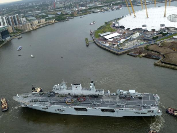 Ein graues Kriegsschiff fährt auf einem Fluss mit der O2 Arena im Hintergrund.