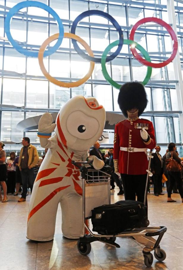 Das Maskottchen der Olympischen Spiele steht neben einer königlichen Wache unter den olympischen Ringen.