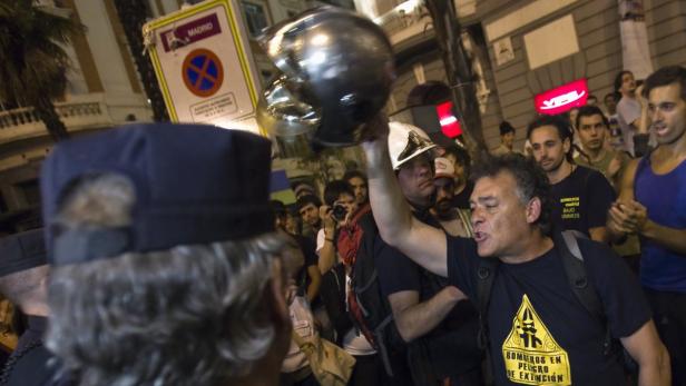 Eine Menschenmenge protestiert in Madrid, einige tragen Feuerwehrhelme.