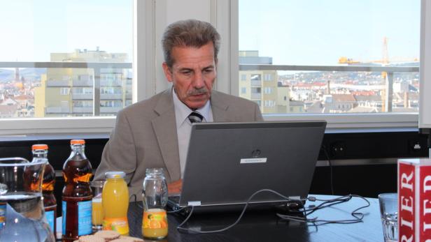 Ein Mann im Anzug sitzt vor einem Laptop mit Blick auf eine Stadt.