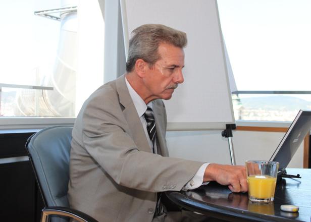 Ein Mann im Anzug sitzt an einem Tisch mit Laptop und einem Glas Orangensaft.