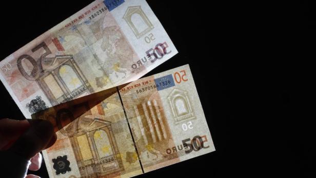 Eine Hand hält einen 50-Euro-Schein vor zwei 20-Euro-Scheinen.