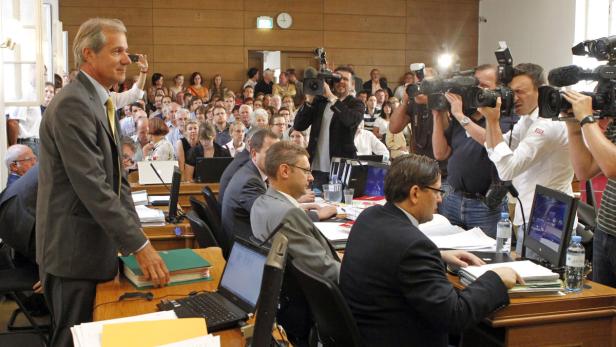 Ein Mann in einem Anzug steht vor einer Gruppe von Menschen und Kameraleuten.