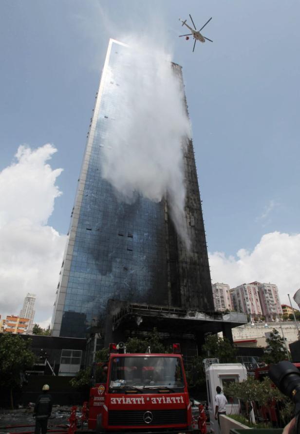 Ein Hochhaus steht in Flammen, während ein Hubschrauber Wasser darüber abwirft.