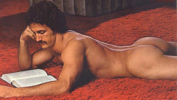 Ein Mann liegt nackt auf einem roten Teppich und liest ein Buch.