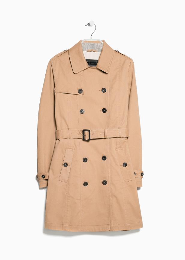 Ein beiger Trenchcoat hängt an einem Kleiderbügel vor einem weißen Hintergrund.