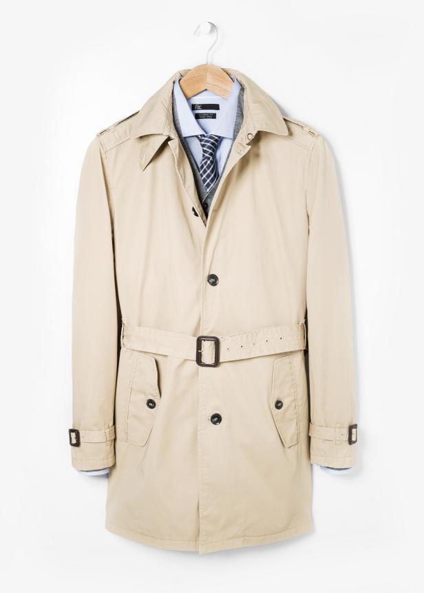 Ein beiger Trenchcoat hängt an einem Kleiderbügel vor einem weißen Hintergrund.