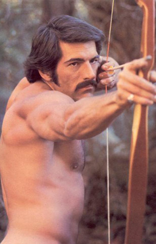 Ein Mann mit nacktem Oberkörper zielt mit Pfeil und Bogen.