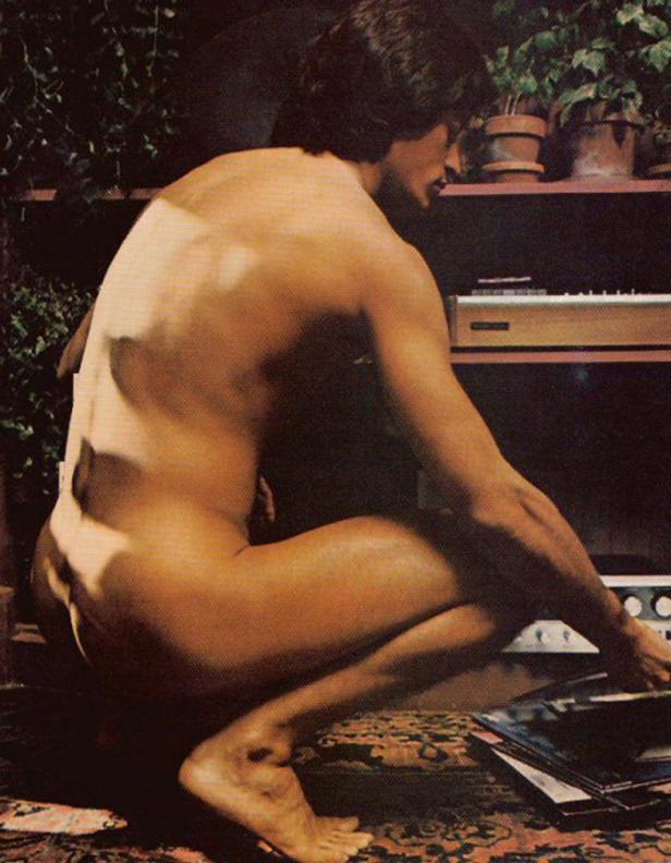 Ein nackter Mann hockt auf einem Teppich und sortiert Schallplatten vor einer Musikanlage.