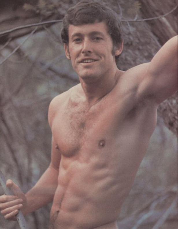 Ein Mann mit freiem Oberkörper posiert vor einem Baum.