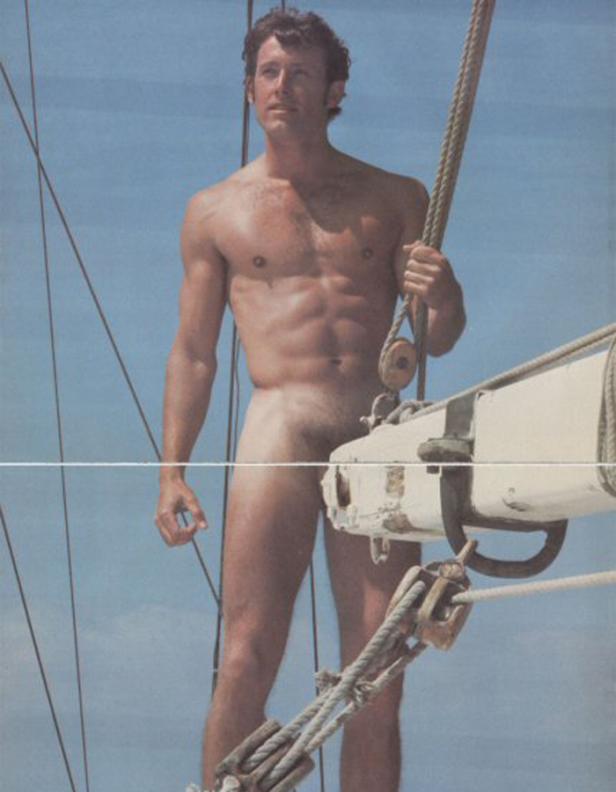 Ein Mann steht nackt auf einem Segelboot vor blauem Himmel.