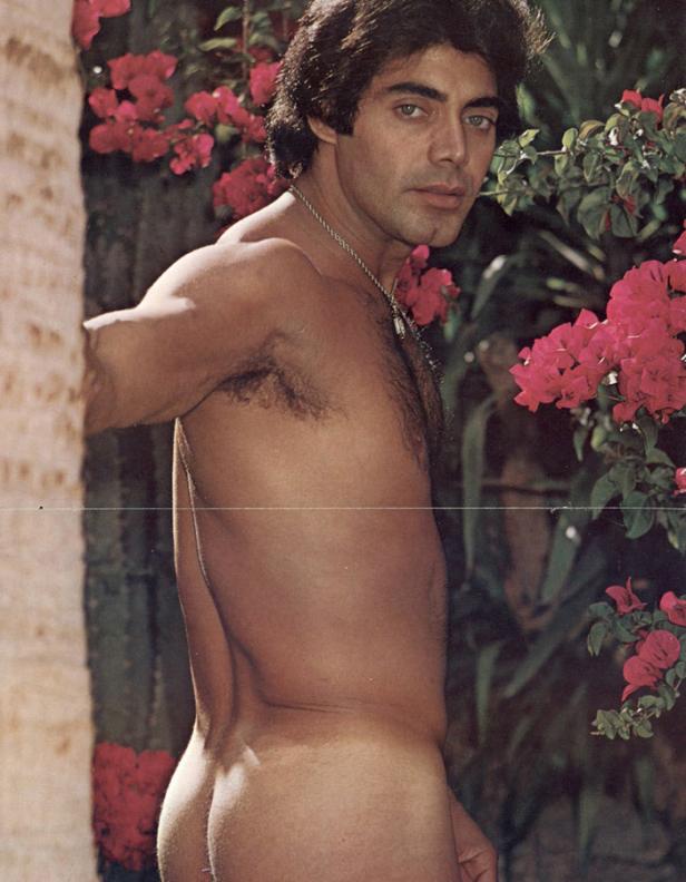 Ein barfüßiger Mann steht neben einer Wand mit rosa Blumen.