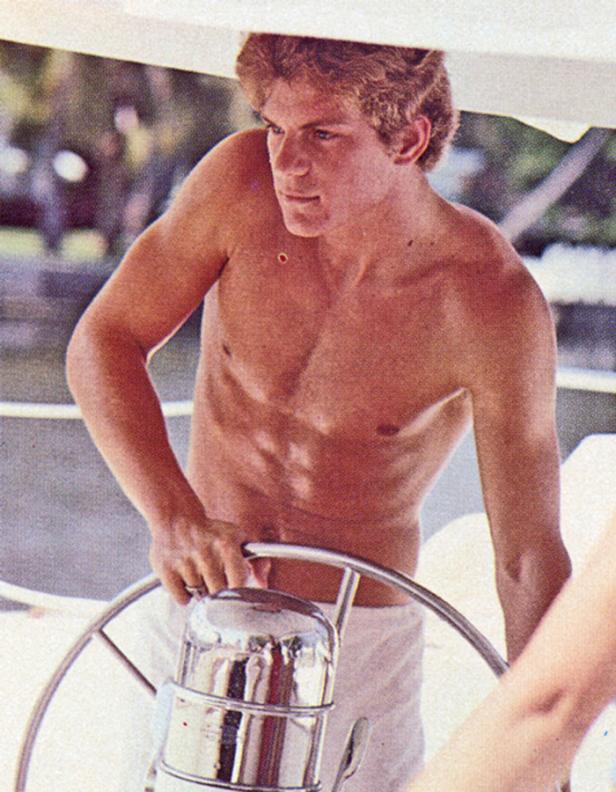 Ein junger Mann ohne Hemd steuert ein Boot.