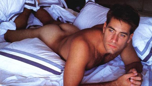 Ein Mann liegt unbekleidet auf einem Bett mit weißer Bettwäsche.