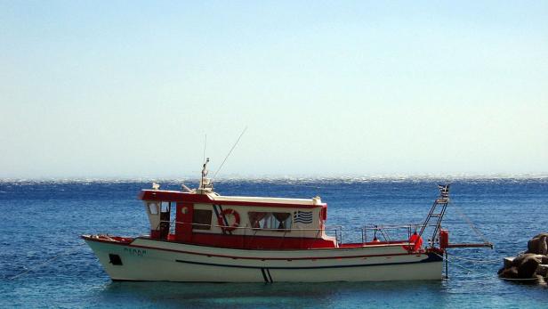 Ein rot-weißes Boot ankert vor einer felsigen Küste im blauen Wasser.