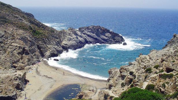 Eine kleine Bucht mit Strand und Badegästen, umgeben von felsigen Klippen.