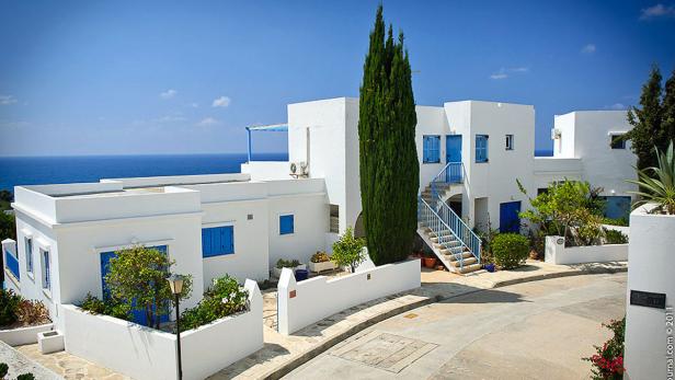 Weiße Häuser mit blauen Fensterläden und Treppen unter blauem Himmel am Meer.
