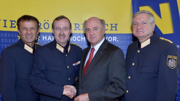 Ein Mann im Anzug schüttelt die Hand eines Polizisten vor einem Hintergrund mit österreichischen Farben.