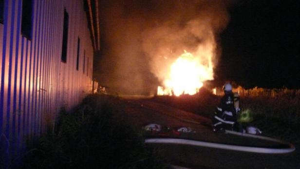 Ein Feuerwehrmann steht vor einem brennenden Gebäude im Dunkeln.