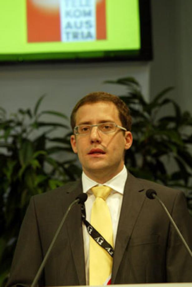 Ein Mann mit Brille und gelber Krawatte spricht an einem Rednerpult.