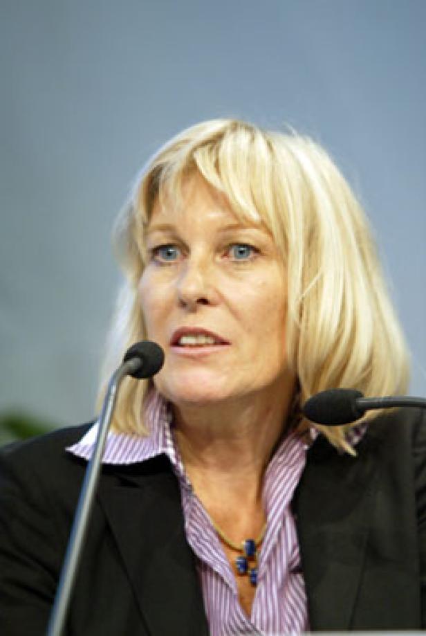 Eine blonde Frau spricht bei einer Konferenz in ein Mikrofon.