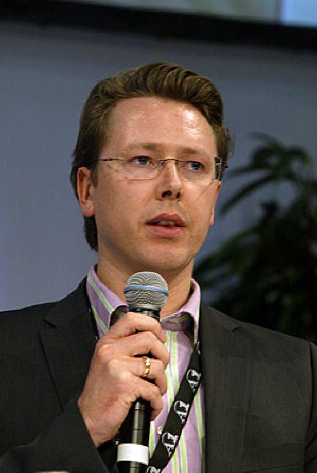 Ein Mann mit Brille hält ein Mikrofon und spricht.