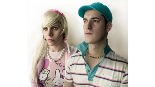 Ein Paar im farbenfrohen 2000er-Jahre-Stil posiert vor einem weißen Hintergrund.