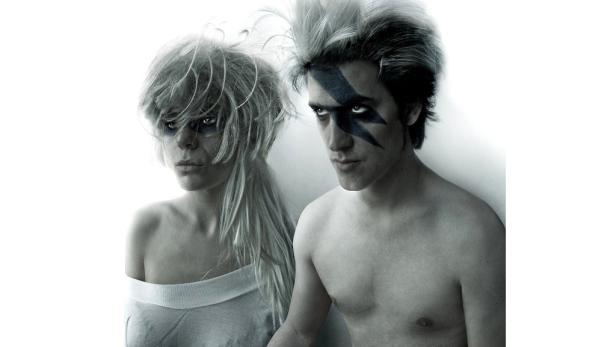 Ein Mann und eine Frau mit blauen Blitz-Gesichtsbemalungen posieren vor einer weißen Wand.