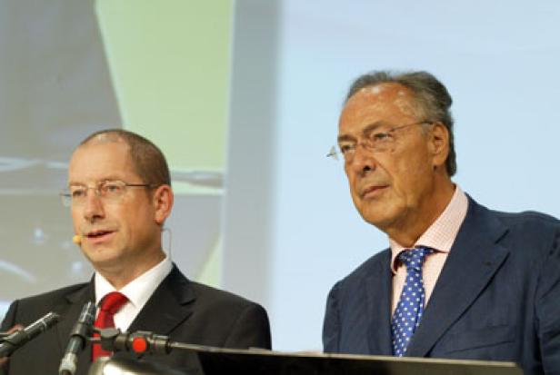 Zwei Männer stehen bei einer Konferenz vor Mikrofonen.