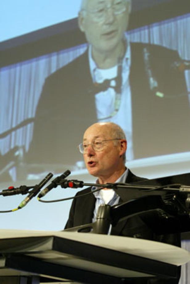 Ein Mann mit Brille hält eine Rede vor einem Publikum.