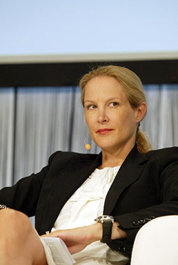 Eine blonde Frau in einem schwarzen Blazer sitzt und hält ein Dokument.