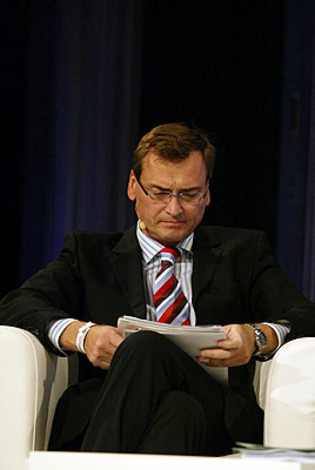 Ein Mann mit Brille und Anzug sitzt in einem Sessel und liest Papiere.