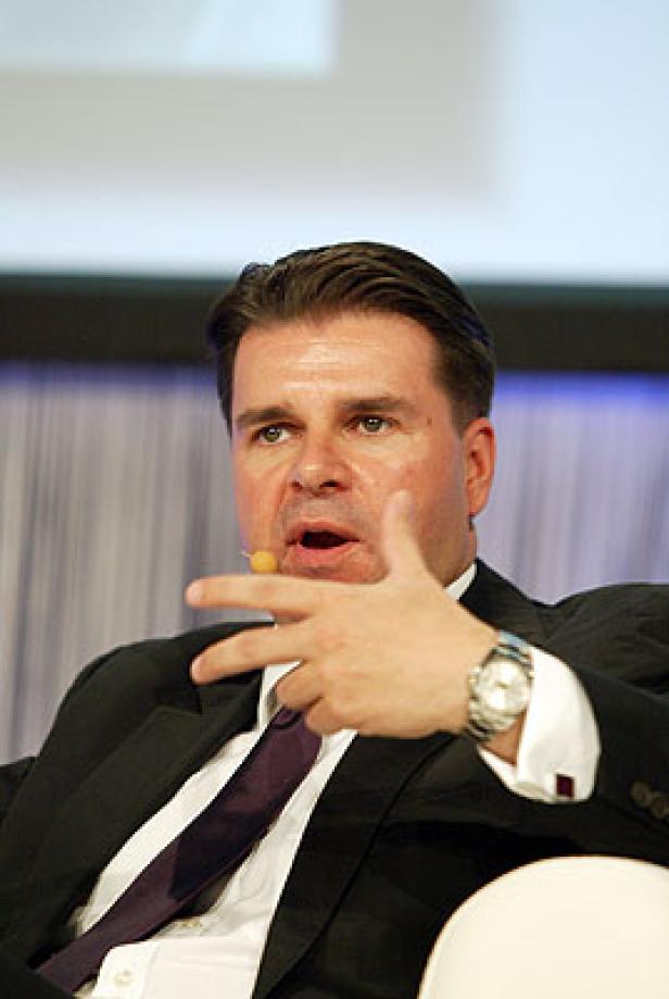 Ein Mann in Anzug und Krawatte gestikuliert während einer Präsentation.